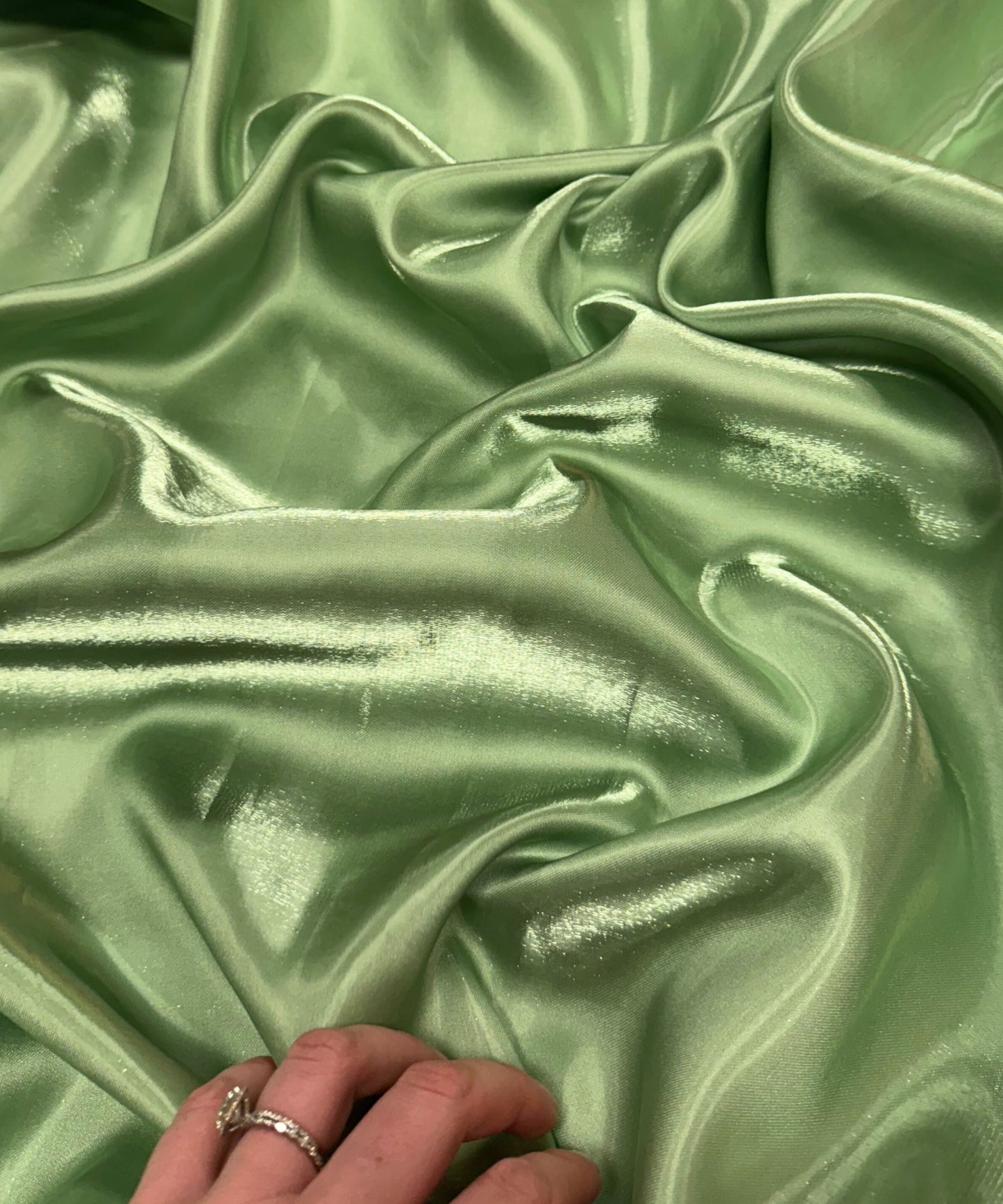 Sage green liquid bridal satin fabric with ultra-glossy finish, fluid drape, and silky smooth texture – perfect for gowns and elegant décor.