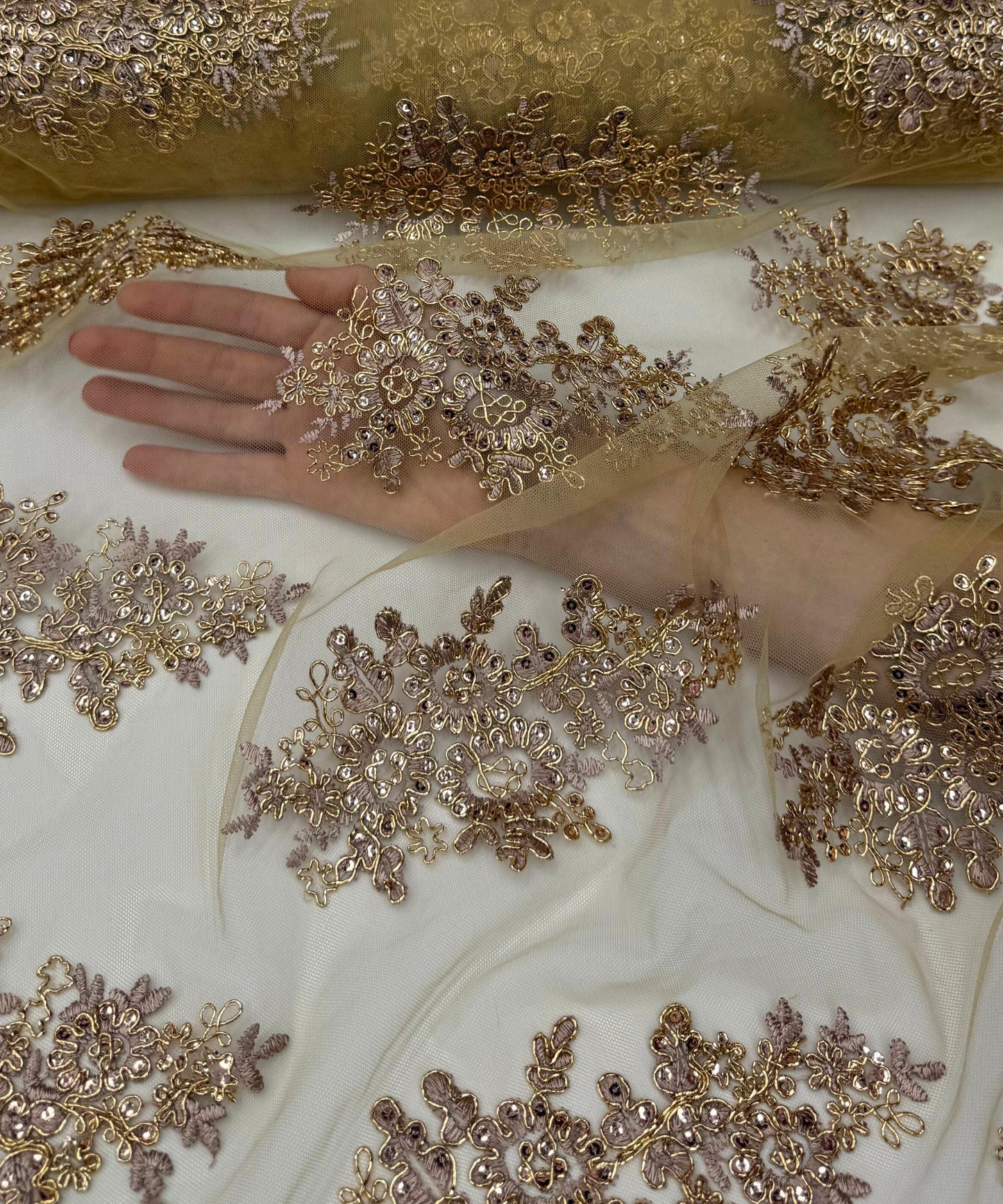 yard of rose gold floral lace fabric with gold embroidery and sequins, detailing the intricate floral patterns and the mesh texture.