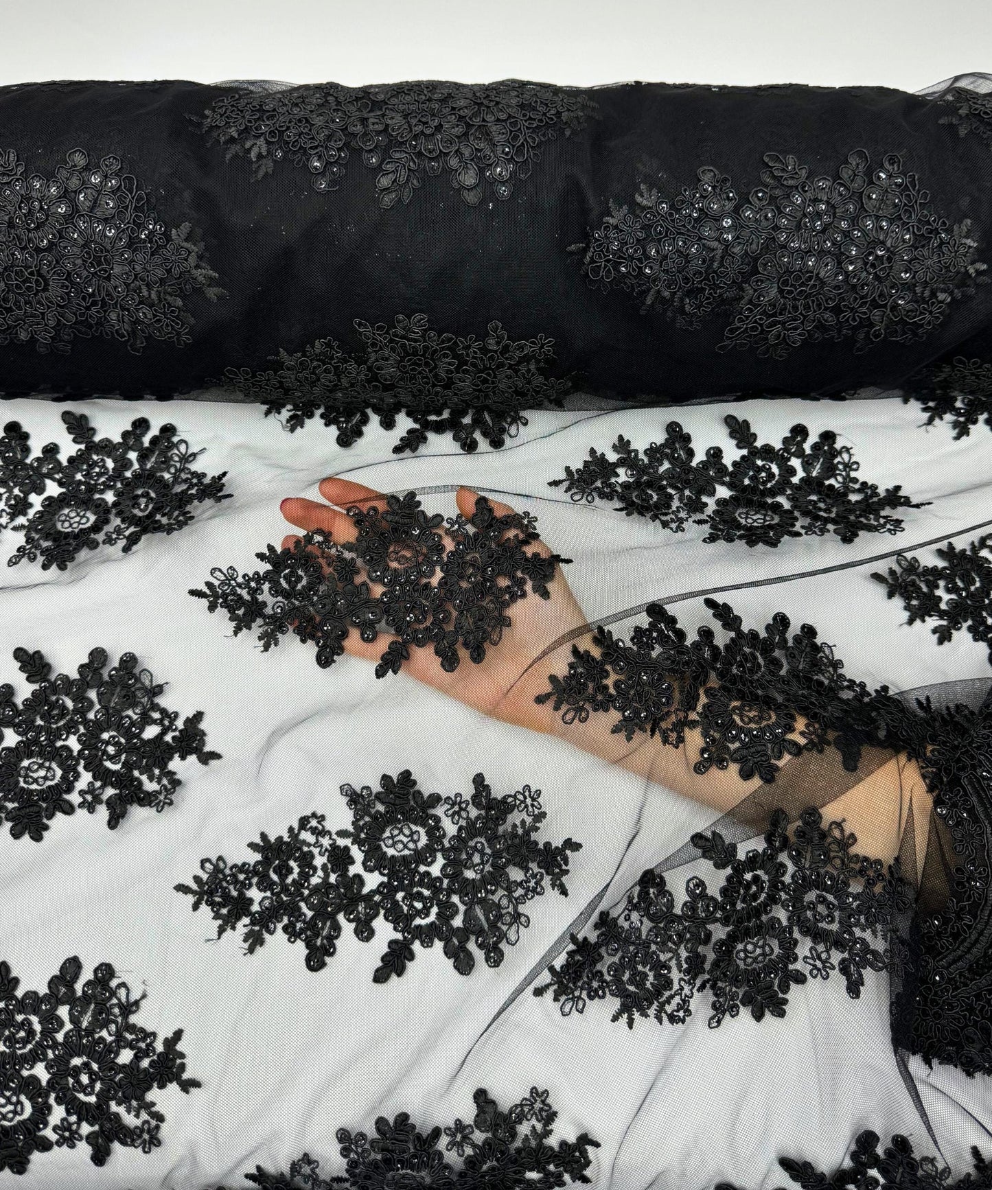yard of black floral lace fabric with gold embroidery and sequins, detailing the intricate floral patterns and the mesh texture.