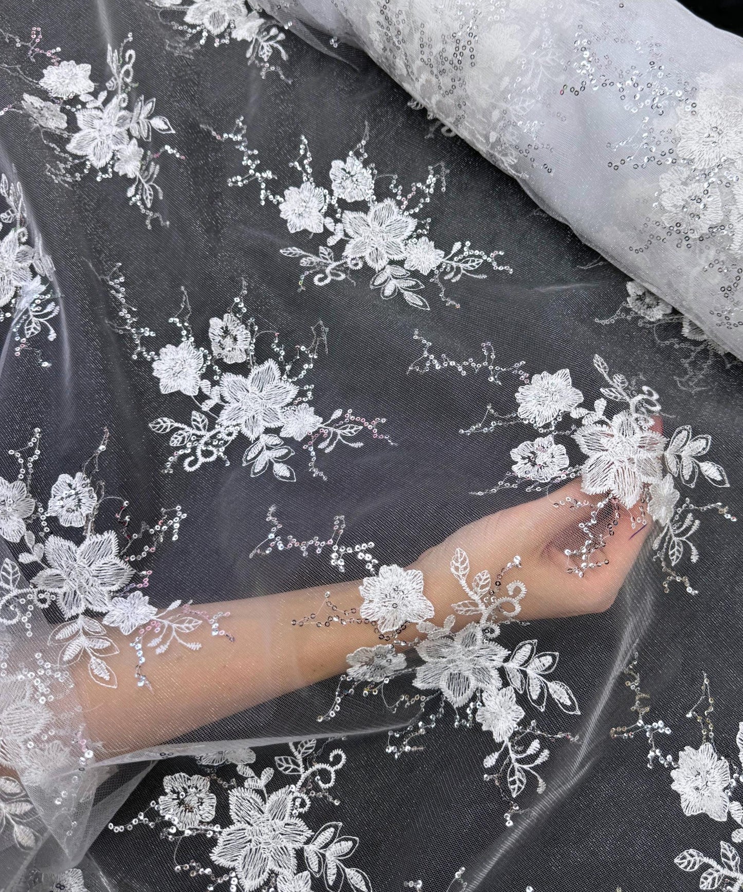 yard of white floral lace fabric with gold embroidery and sequins, detailing the intricate floral patterns and the mesh texture.