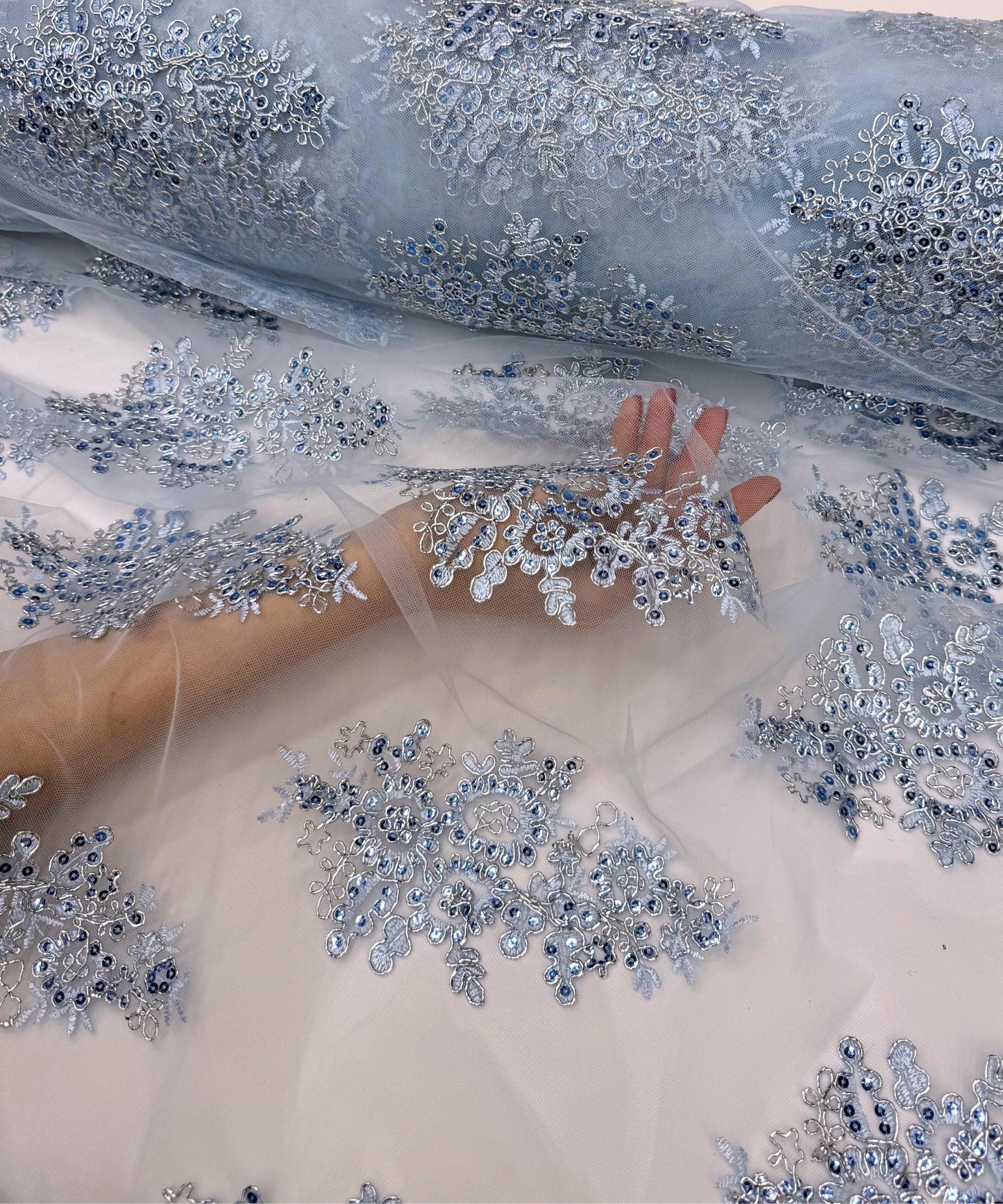 yard of light blue floral lace fabric with gold embroidery and sequins, detailing the intricate floral patterns and the mesh texture.