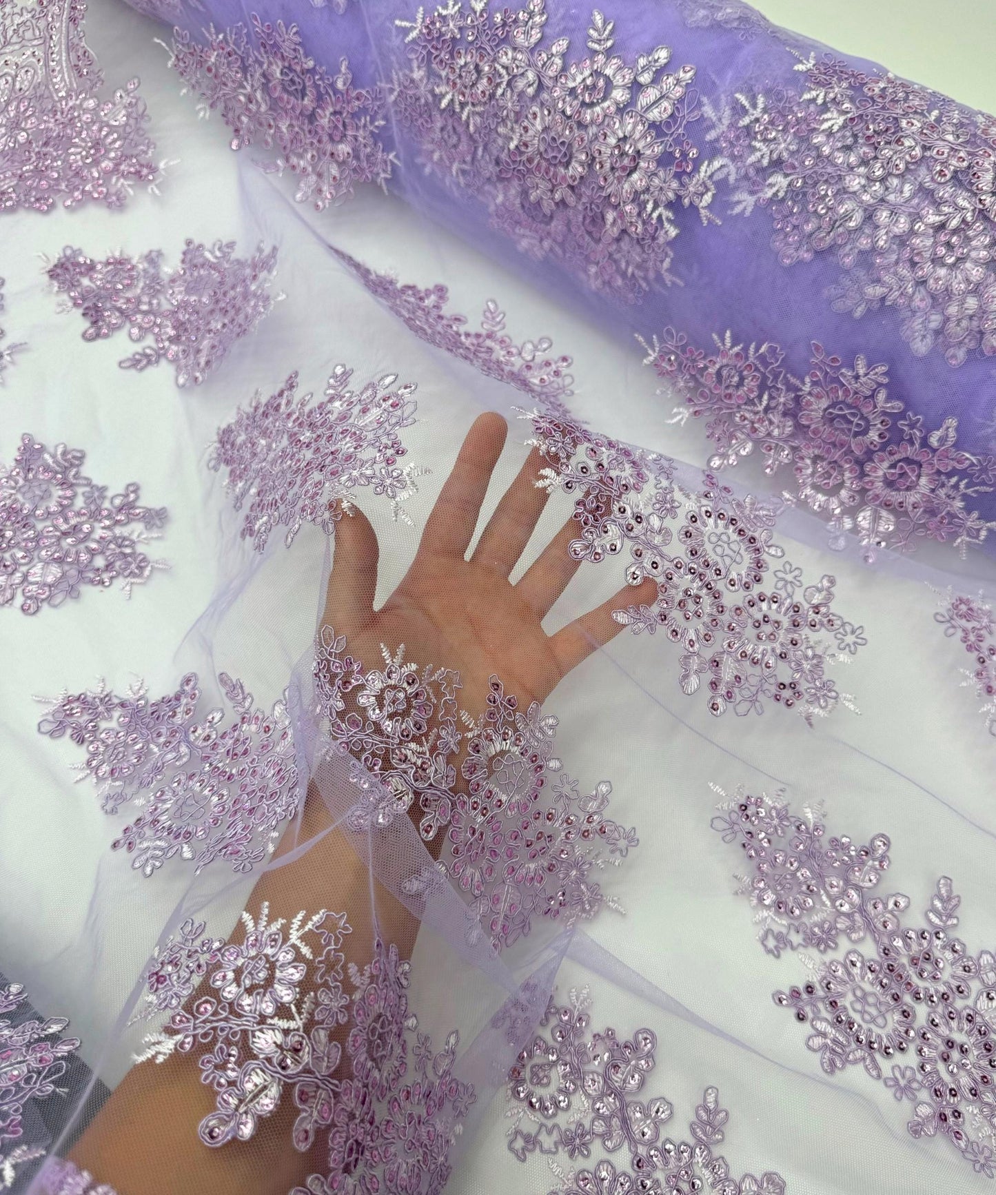 yard of lilac floral lace fabric with gold embroidery and sequins, detailing the intricate floral patterns and the mesh texture.
