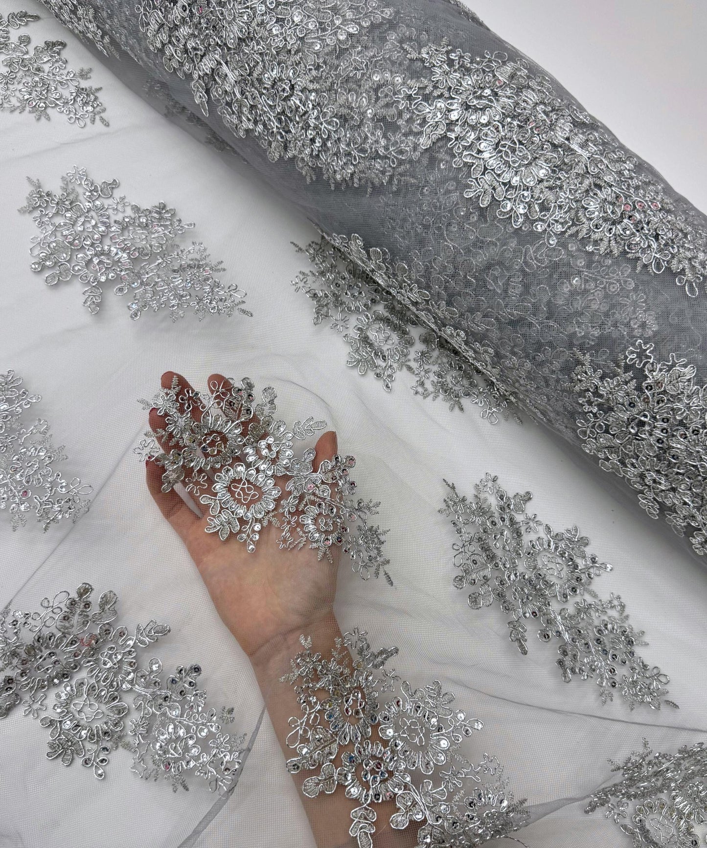 yard of silver floral lace fabric with gold embroidery and sequins, detailing the intricate floral patterns and the mesh texture.